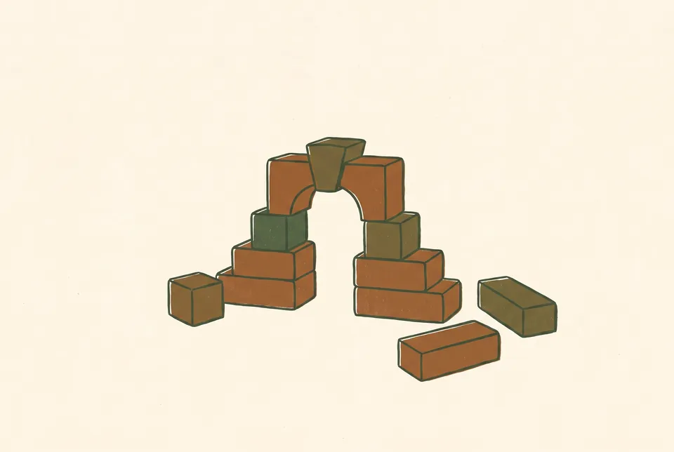 Blank building blocks stacked into a small arch, with a few spare blocks on the ground.